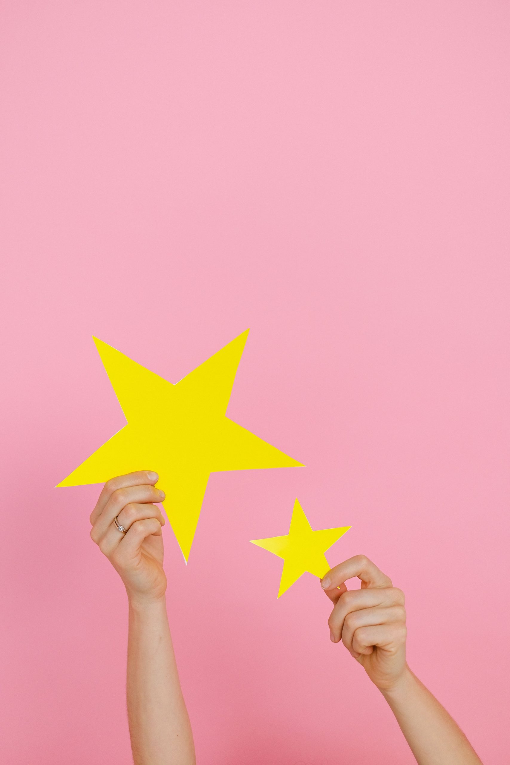 Close-up of hands holding yellow star shapes against a pink background.
